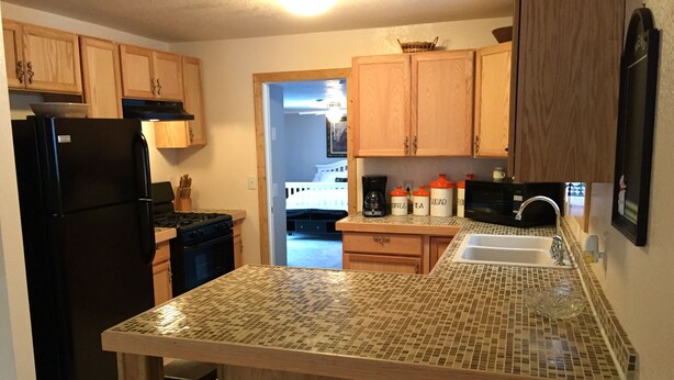 A kitchen with wooden cabinets, a black refrigerator, a stove, a microwave, and a sink with a tiled backsplash. - Open All Year. Ausable River Access. Newly Remodeled! (Roscommon)
