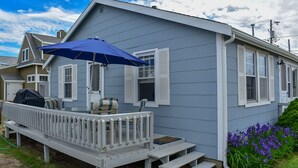 A house with a covered porch, a grill, and a small garden with purple flowers.