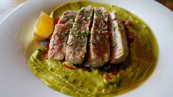 A plate of food with sliced meat, vegetables, and a green sauce.