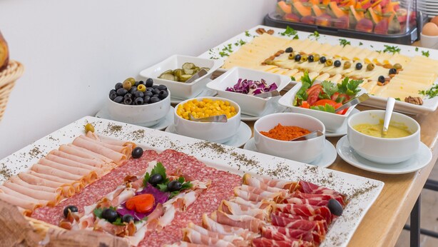 Una mesa de buffet con diversos alimentos, entre ellos carnes, quesos y frutas.