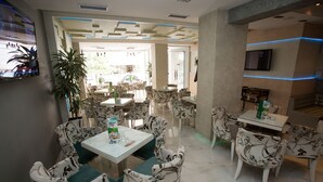 Un restaurante moderno con sillas y mesas de estampado floral, un televisor de pantalla plana y una zona de estar con vistas a la calle.