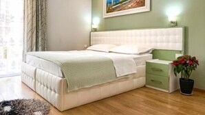 Un dormitorio con cama, mesitas de noche, una planta en maceta y un cuadro en la pared.