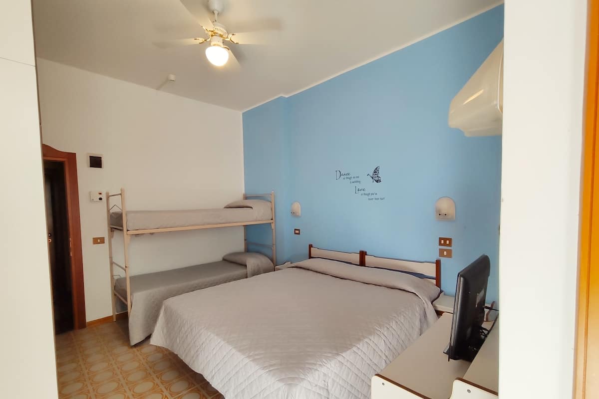 Une chambre avec des lits superposés, un bureau, un ventilateur de plafond et un mur orné d’une citation inspirante.