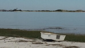 En liten båt som heter SALTY ligger på en sandstrand, och i bakgrunden syns ett lugnt vatten och en avlägsen fyr.