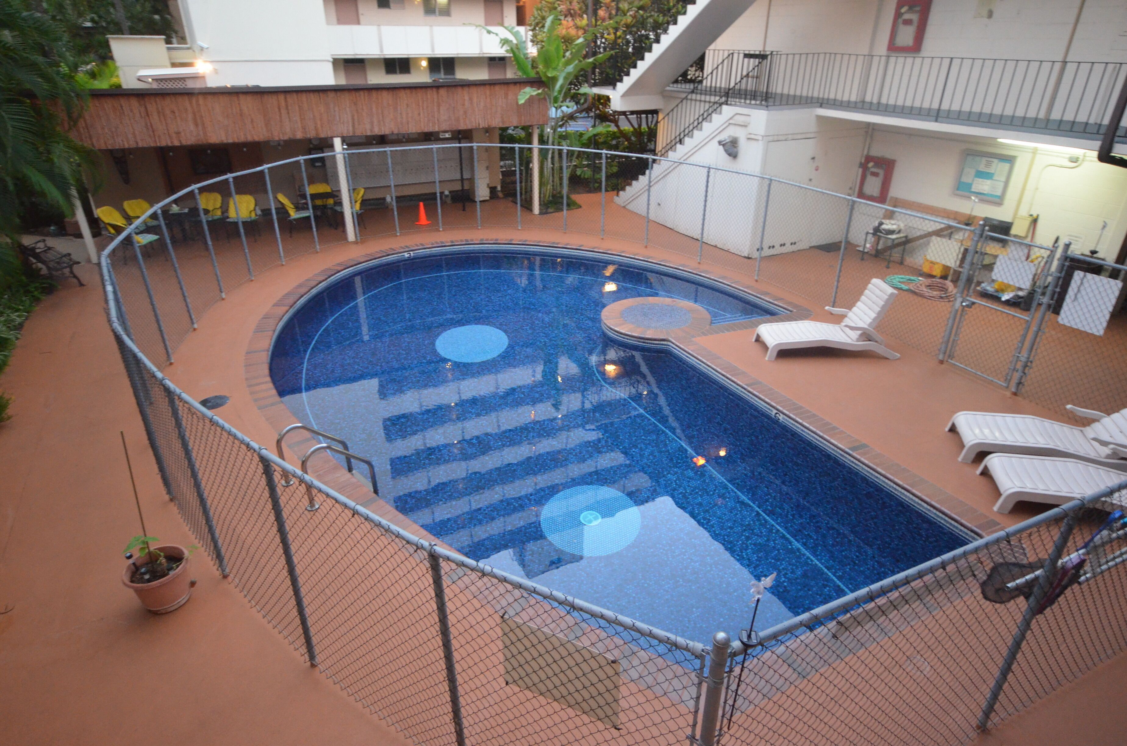 An outdoor swimming pool with a fenced area, lounge chairs, and a staircase leading to an upper level.