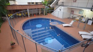 Piscina exterior con área cercada, sillas de descanso y una escalera que lleva a un nivel superior.
