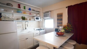 Cocina compacta con armarios blancos, microondas, lavabo y ventana.