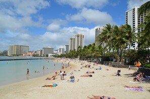 Ein Strand mit Palmen, sonnenbadenden Menschen und hohen Gebäuden im Hintergrund.