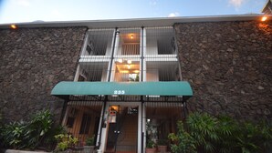 Un edificio con fachada de piedra, toldo verde y una entrada visible con una escalera que lleva a un nivel superior.