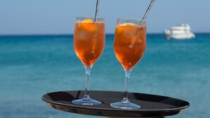 Two glasses of orange beverage on a black tray with a ship in the background. - Aegon Mykonos, Autograph Collection (Mykonos)