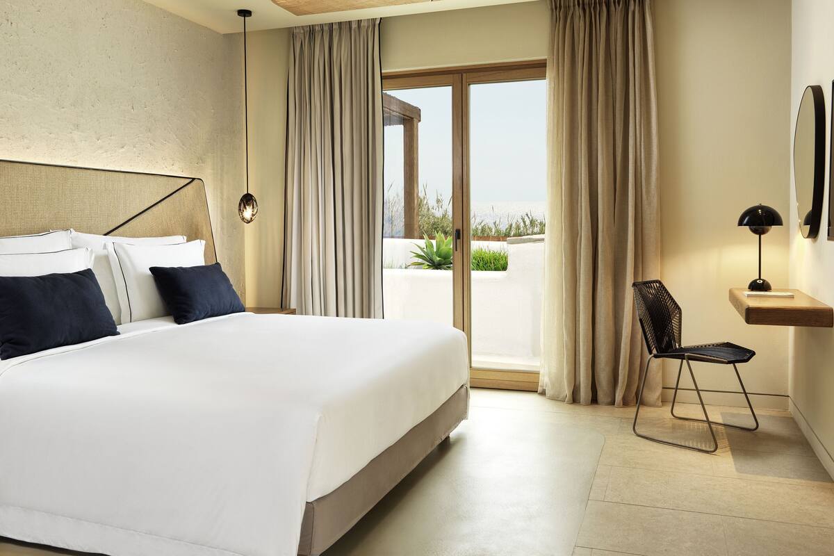 A modern hotel room with a large bed, a desk, and a view of the outdoors.