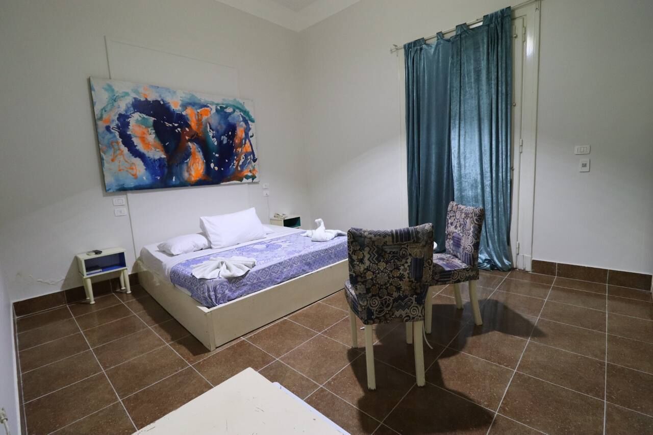 A bedroom with a bed, a chair, a painting, and a curtain.