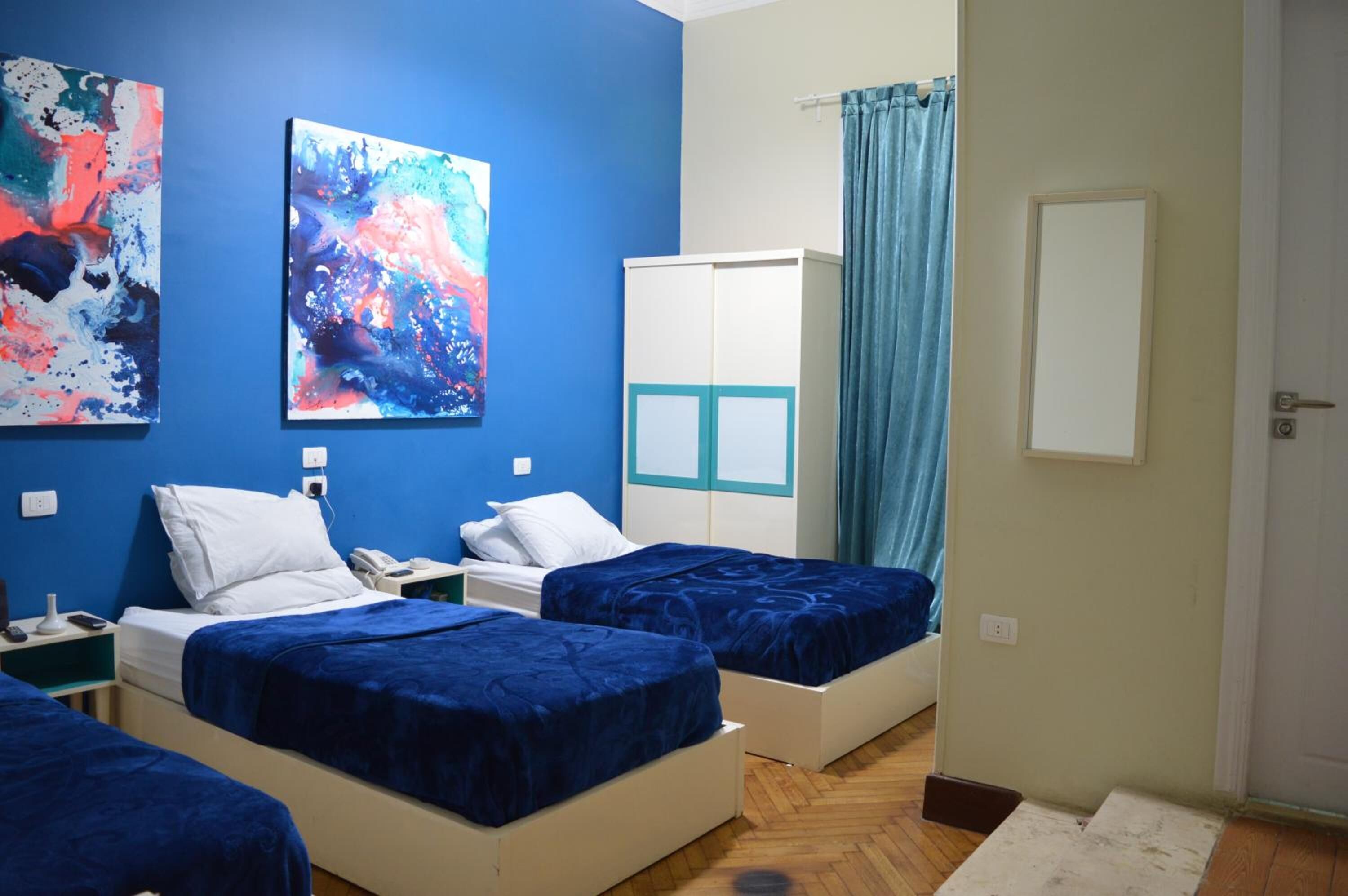 A room with two beds, a wardrobe, and abstract paintings on the wall.