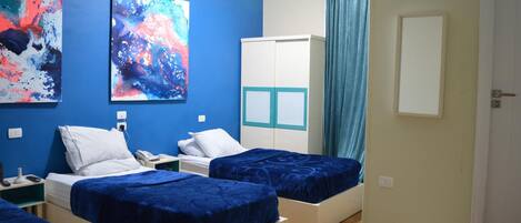 A room with two beds, a wardrobe, and abstract paintings on the wall.