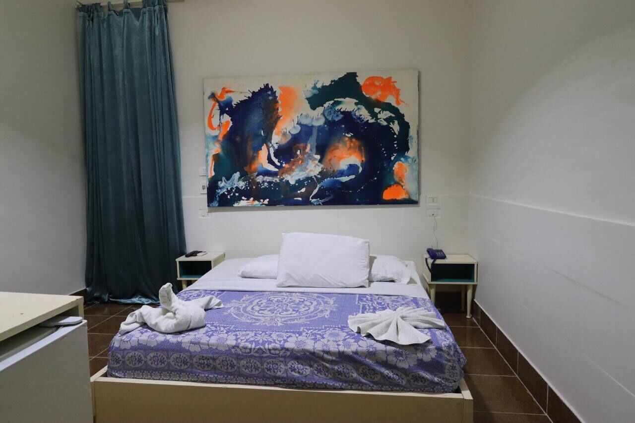 Una habitación de hotel con una cama, una mesita de noche, un escritorio y un cuadro abstracto grande en la pared.