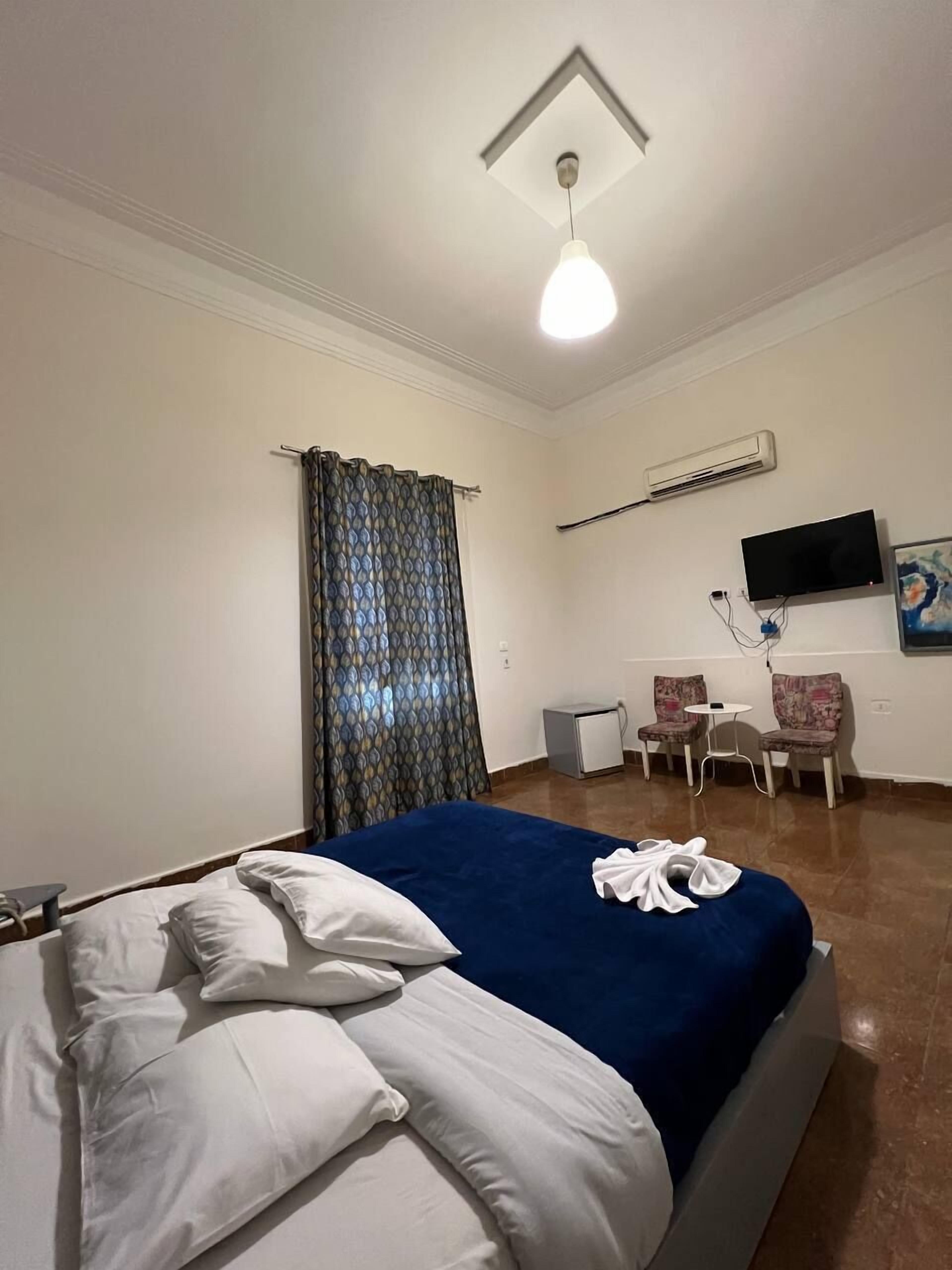 A hotel room with a bed, a desk, a chair, an air conditioning unit, and a television.