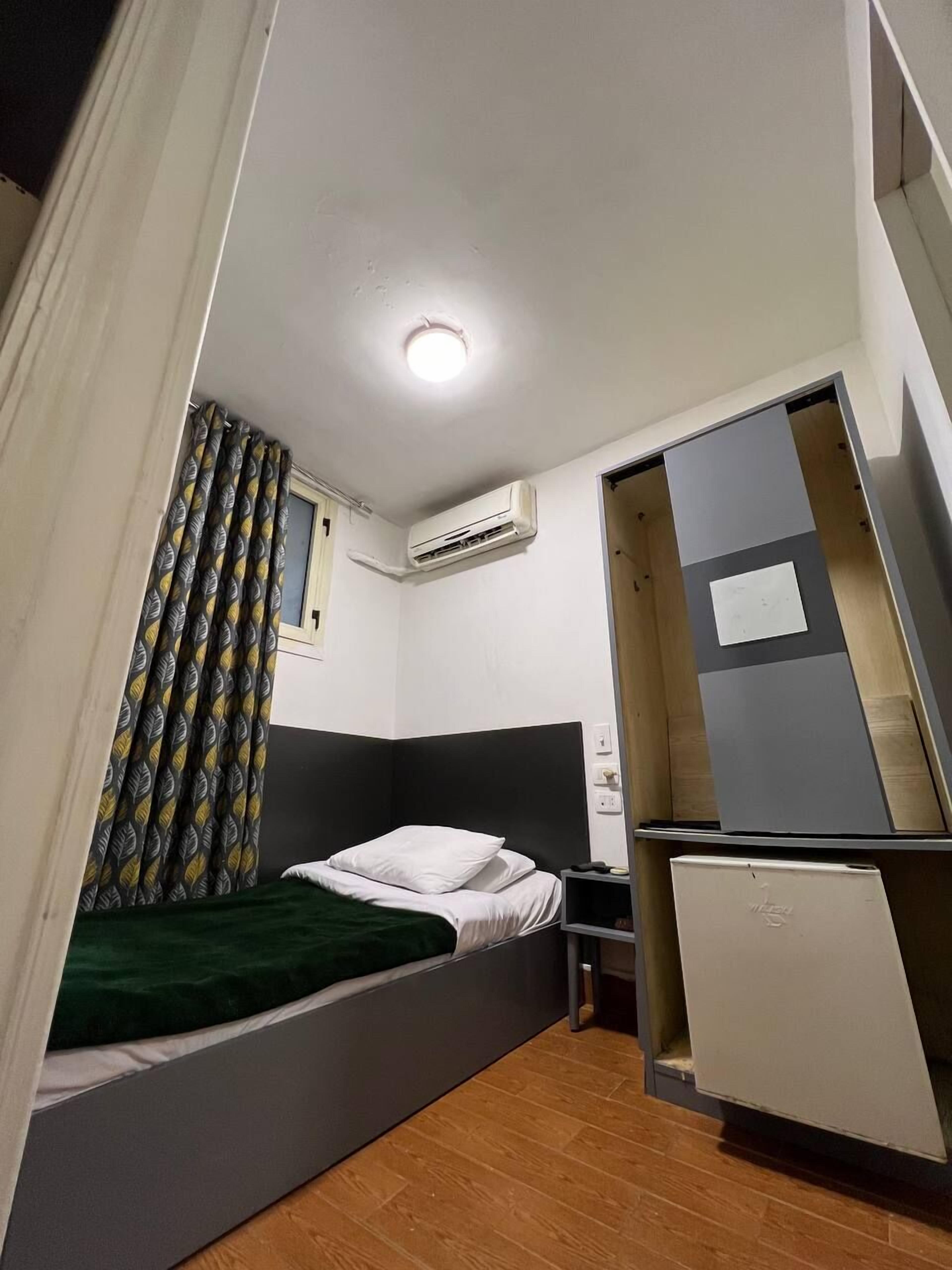 Et lille værelse med seng, skrivebord, aircondition og garderobeskab.