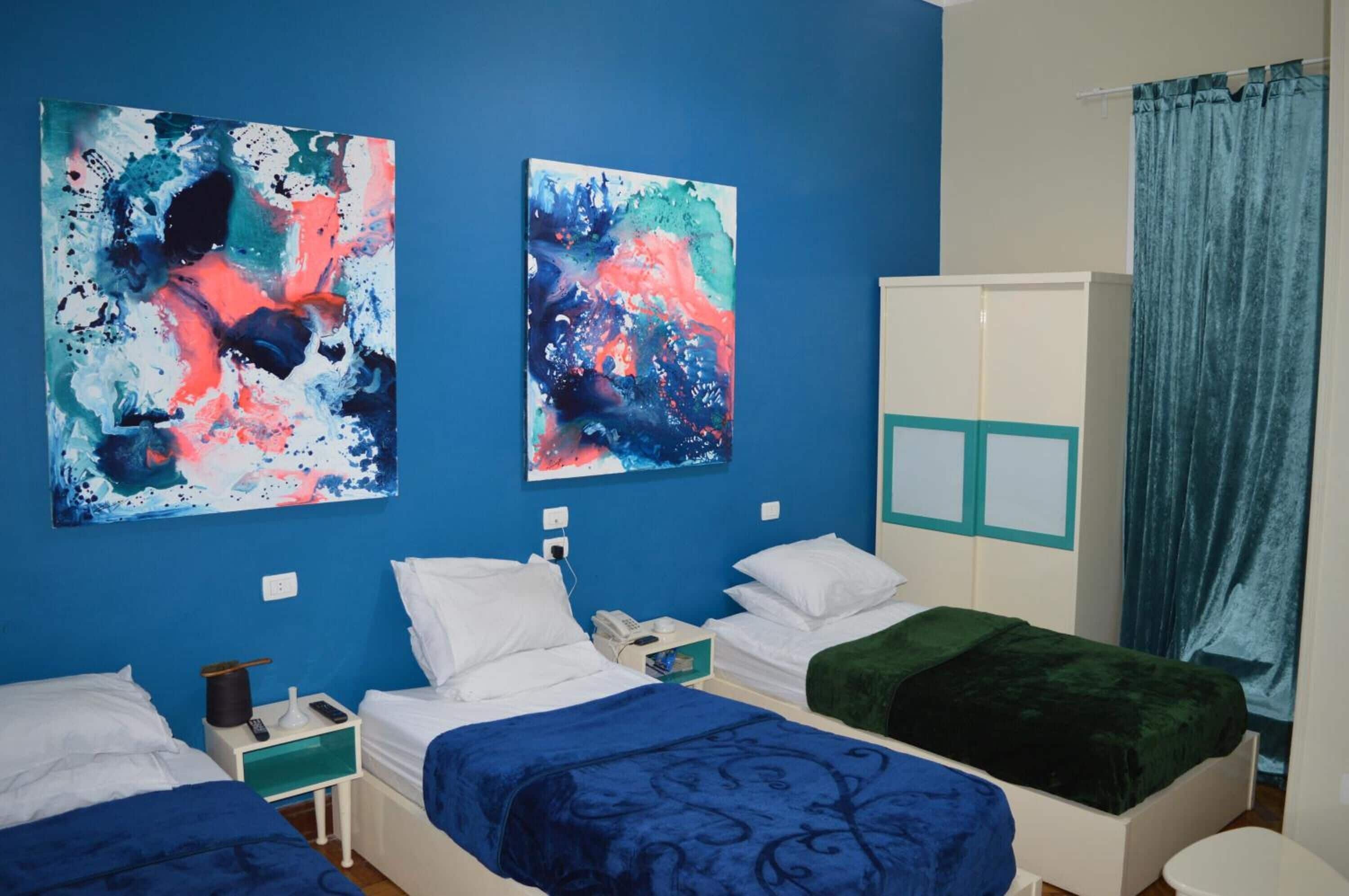 A hotel room with two beds, a wardrobe, and abstract paintings on the wall.