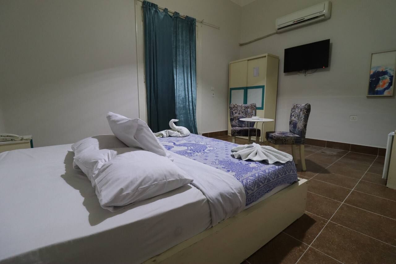 A hotel room with a bed, a chair, a television, and an air conditioning unit.