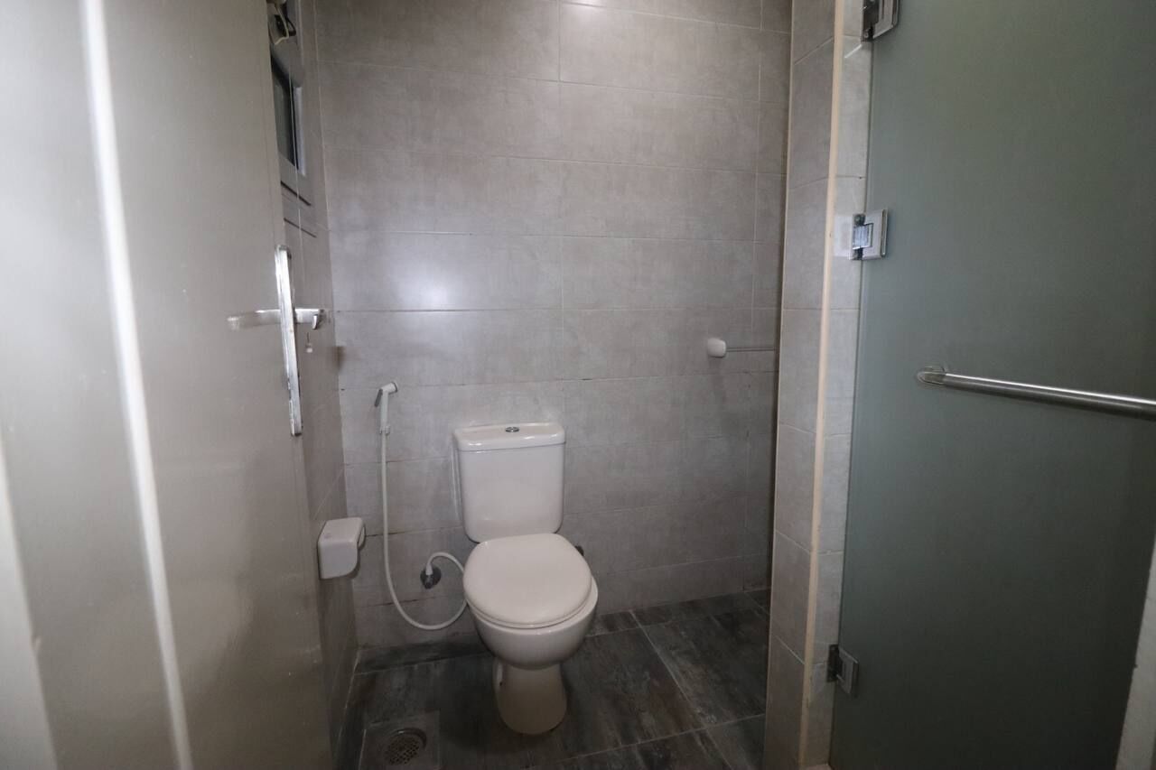 A small, enclosed bathroom with a toilet, a hand dryer, and a wall-mounted light fixture.