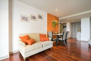 Een moderne woonkamer met een bank, eettafel en stoelen. Er hangen afbeeldingen in lijsten aan de muur en staat een vaas met bloemen.
