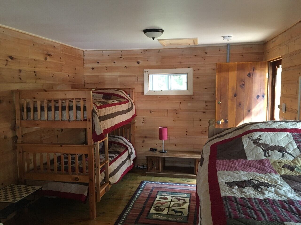 A cabin with bunk beds, a small table, a lamp, and a quilt with animal prints.