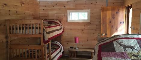 A cabin with bunk beds, a small table, a lamp, and a quilt with animal prints.