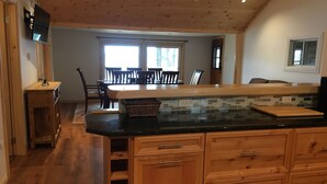 A kitchen with wooden cabinets, a black countertop, and a dining area with a table and chairs. - Loon Lodge - Golden Lake (Cottage & Bunkie -Sleeps 8 ) (Killaloe)