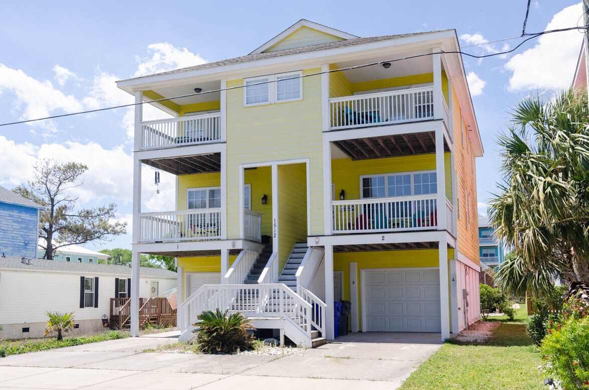 A two-story residential building with a balcony on the second floor, a front garage, and a staircase leading to the entrance.