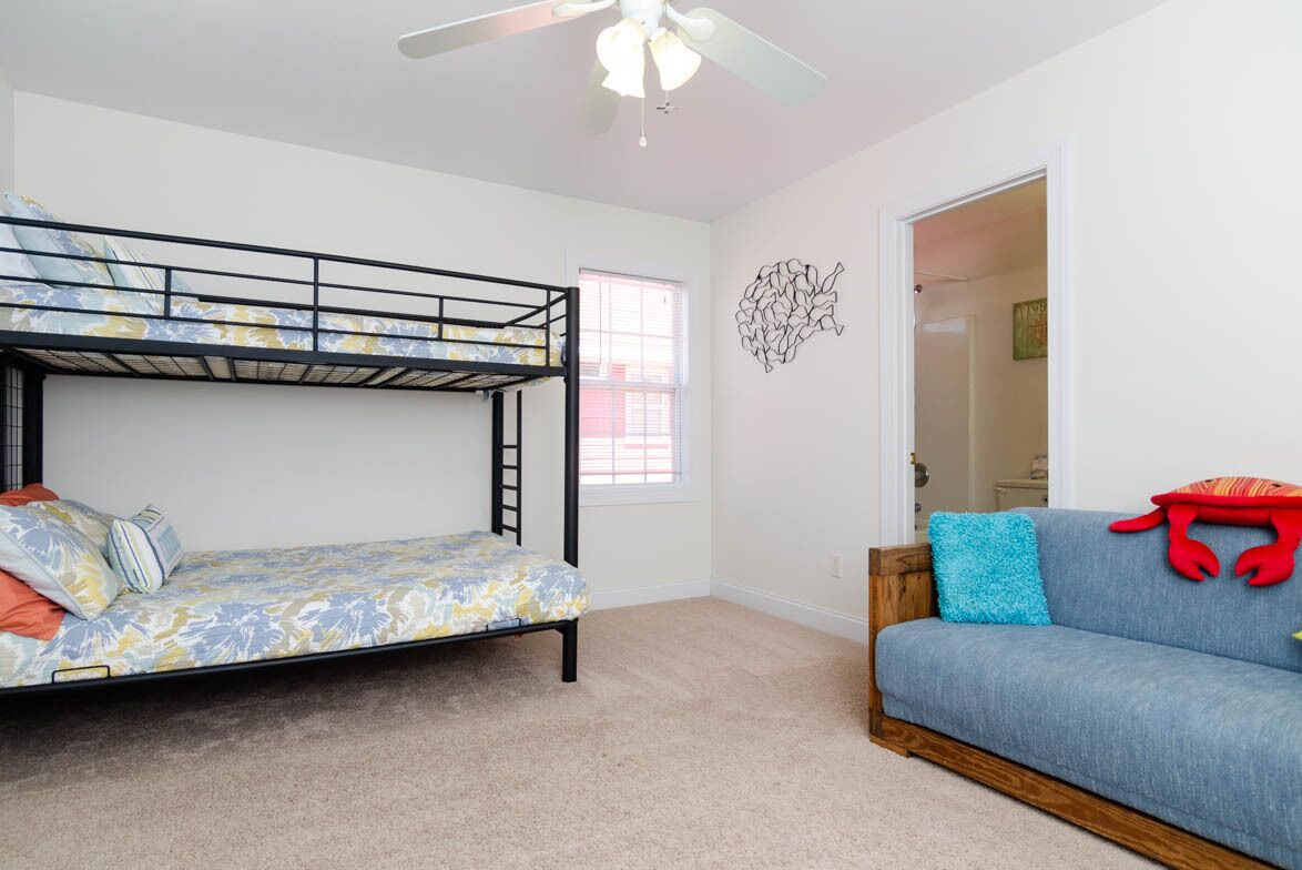 Une chambre avec un lit superposé, un canapé, un ventilateur de plafond et une fenêtre.