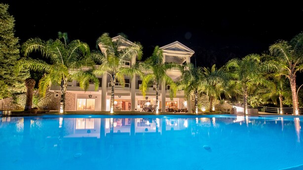 Vista nocturna de un hotel con piscina, palmeras y una fachada de edificio bien iluminada.