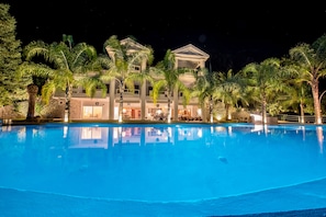 A nighttime view of a hotel with a swimming pool, palm trees, and a well-lit building facade. - Villa Paradizo (Kalamata)