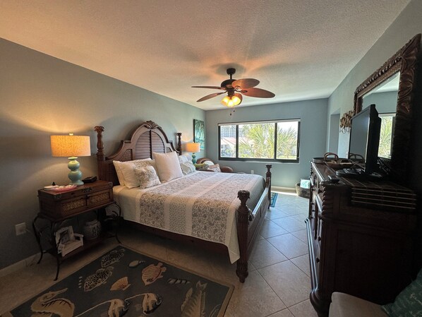 A bedroom with a bed, a desk, a chair, a ceiling fan, a window, and a dresser.