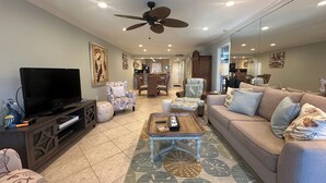 A living room with a television, sofas, chairs, a coffee table, and a ceiling fan.