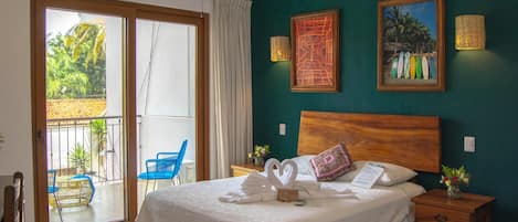 Habitación de hotel con cama, mesita de noche, cabecero de madera, ventana con vista al exterior y pared con dos cuadros enmarcados.