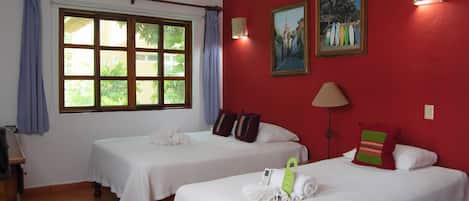 Une chambre d’hôtel avec deux lits, une grande fenêtre avec des rideaux, un tableau et une lampe.