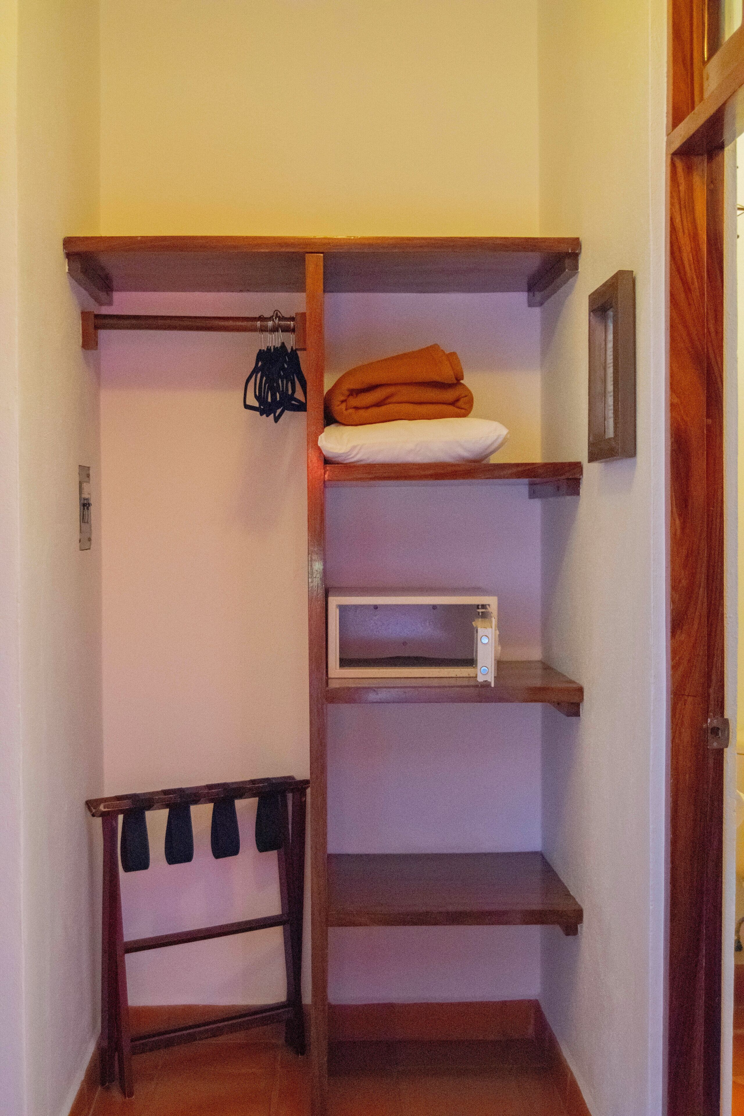 A wooden closet with shelves, a hanging rack, and a microwave.