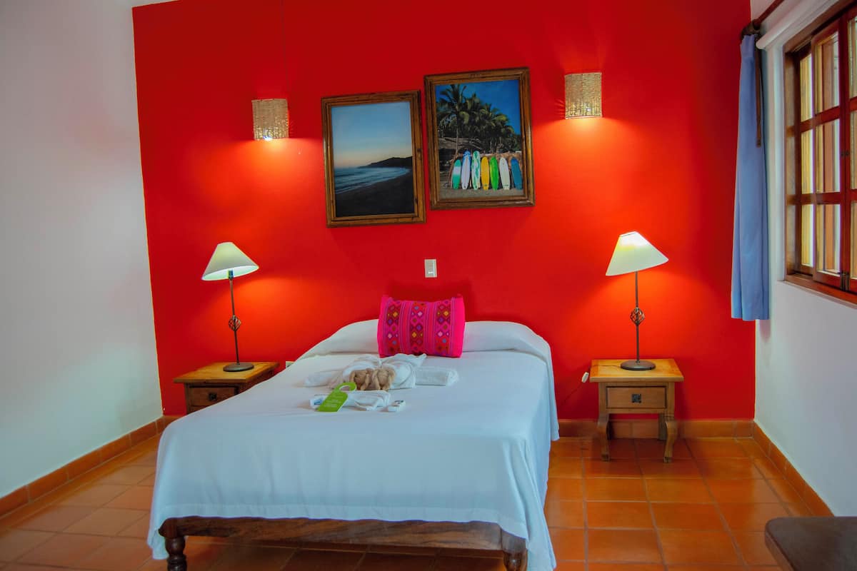 Una habitación de hotel con cama, dos mesitas de noche, una ventana y dos lámparas de pared.