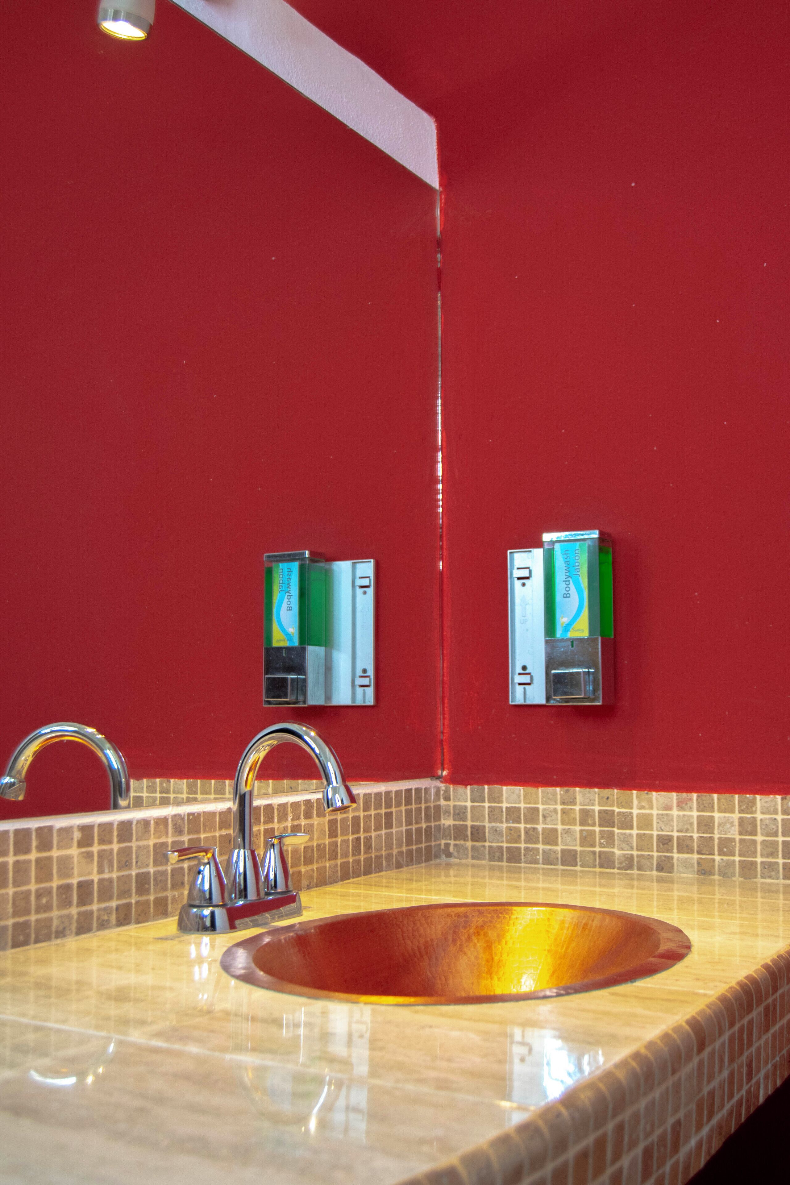 Un baño con una pared roja, un lavabo con espejo y dos dispensadores de jabón.