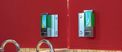 Un baño con una pared roja, un lavabo con espejo y dos dispensadores de jabón.