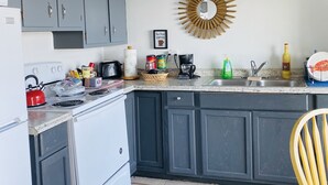 A kitchen with grey cabinets, a white stove, and a sink. There is a yellow chair in the corner. - Lake Front Sebring Villa , Relax- Quiet with Breathtaking views! (Sebring)