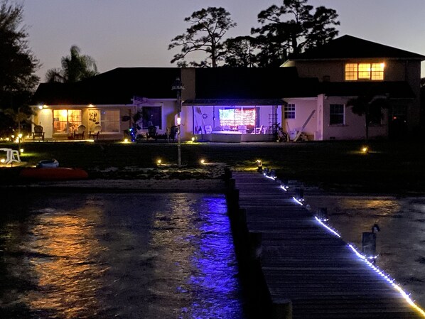 A waterfront property with a dock, outdoor seating, and illuminated windows. - Lake Front Sebring Villa , Relax- Quiet with Breathtaking views! (Sebring)