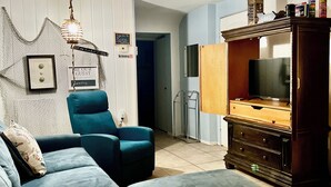 A living room with a dark blue sofa, a wooden cabinet with a TV, and a decorative wall hanging. - Lake Front Sebring Villa , Relax- Quiet with Breathtaking views! (Sebring)