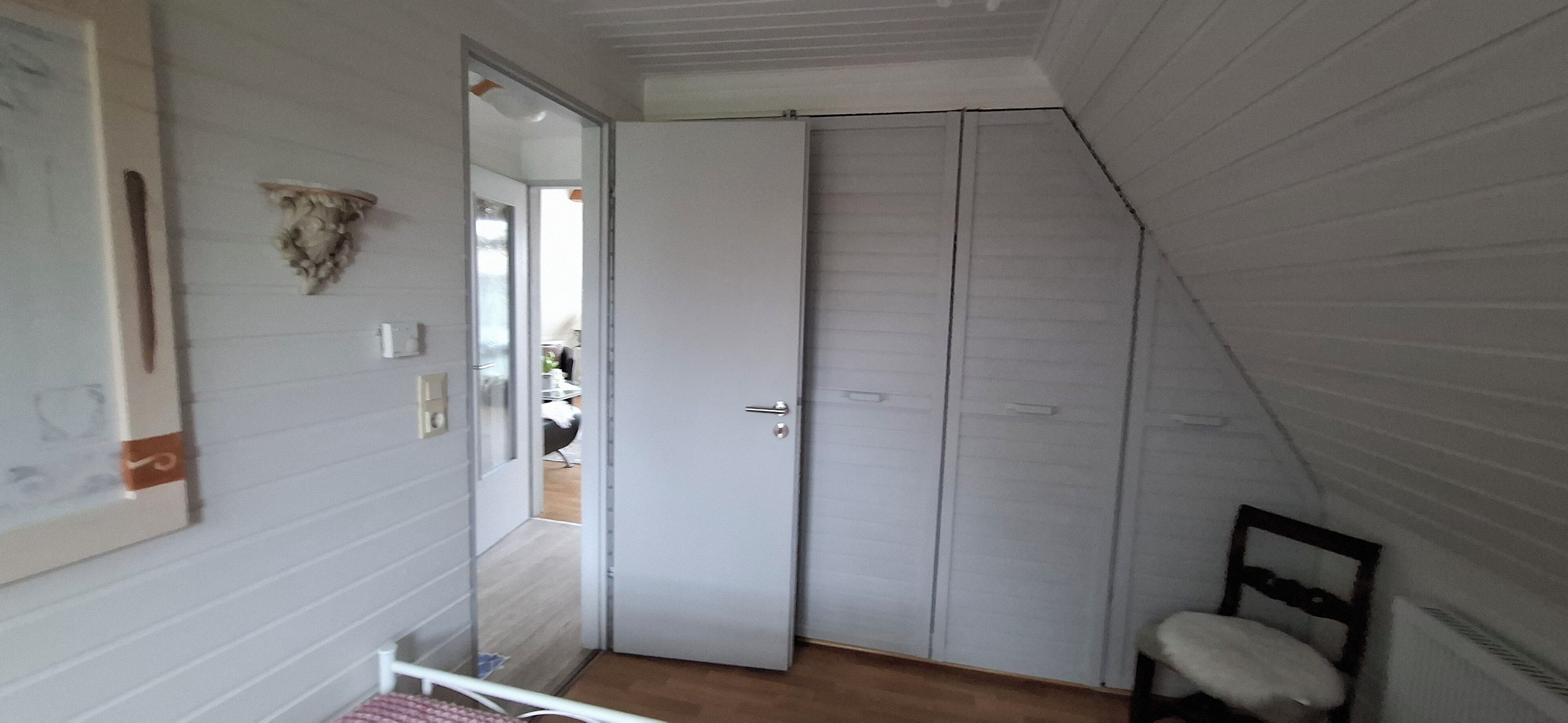 A room with a white wardrobe, a small chair, and a mirror on the wall.