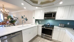 A modern kitchen with white cabinets, stainless steel appliances, and a teal backsplash. - Sanibel Harbour 635:Adventure awaits-Nearby fishing, kayaking, dolphin tours and more! (Fort Myers)