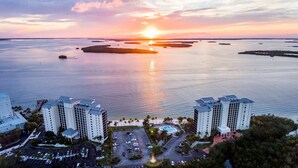 A high-rise hotel with a central courtyard, a swimming pool, and a view of the sunset over a body of water with islands. - Sanibel Harbour 635:Adventure awaits-Nearby fishing, kayaking, dolphin tours and more! (Fort Myers)