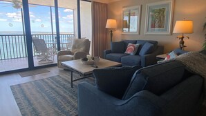 A living room with a sofa, armchair, and coffee table, a balcony with chairs, and a view of the ocean. - Sanibel Harbour 635:Adventure awaits-Nearby fishing, kayaking, dolphin tours and more! (Fort Myers)