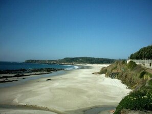 A coastal landscape with a sandy beach, a rocky shoreline, and a cliff with vegetation.