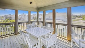 A covered outdoor area with a table and chairs, large windows, and a view of the neighborhood.
