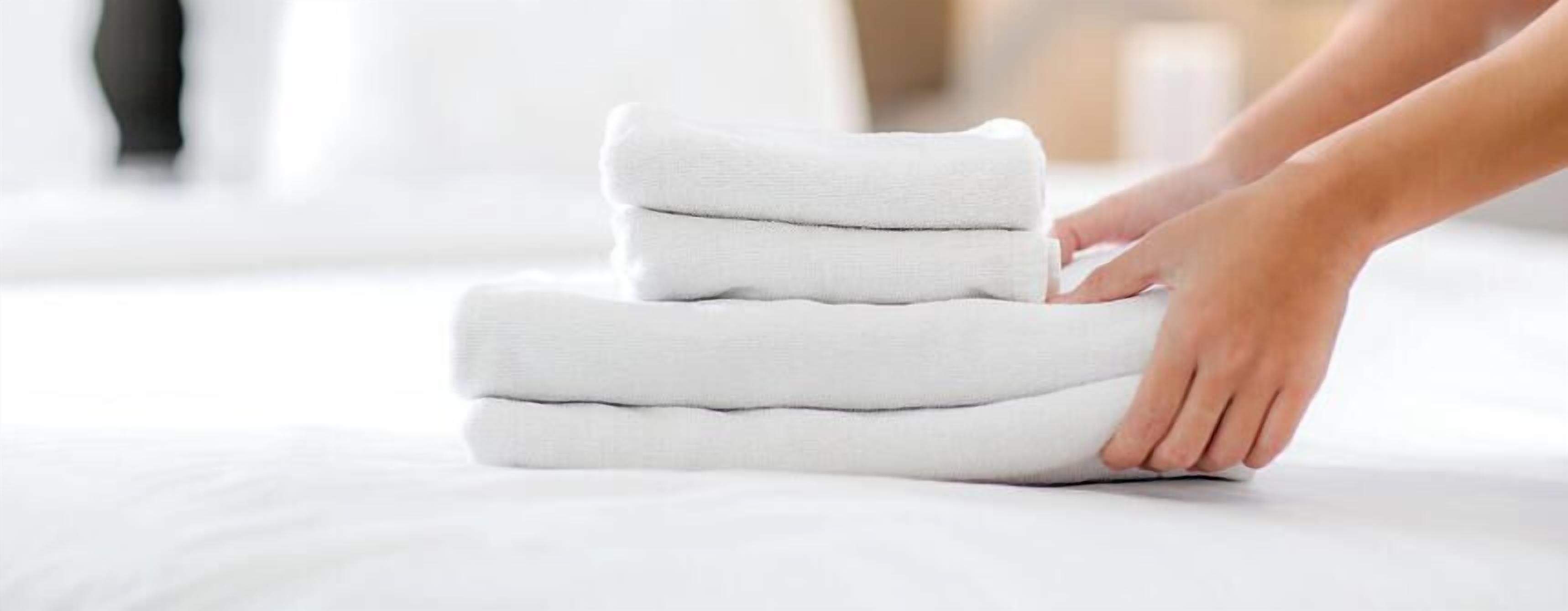 Iemand vouwt een stapel witte handdoeken op een bed.